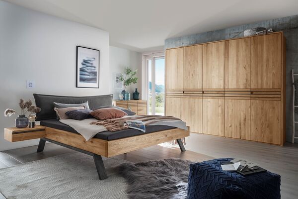 Ein modernes Schlafzimmer mit einem Forestale-Holzbett, eleganter Kommode und großem Kleiderschrank in warmen Holzfarben