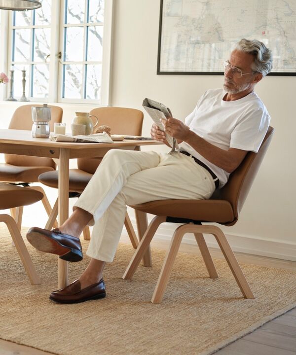 Grauhaariger Mann mit Zeitung am Esstisch sitzend, mit Stressless-Dining-Stühlen in caramel oak