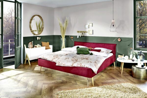 Samtweiches, dunkelrotes Stoffbett von Tasso mit Wasserbettmatratze in einem Raum mit weißen Möbeln, strukturiertem Holzboden und olivgrünen Wänden und Fenstern
