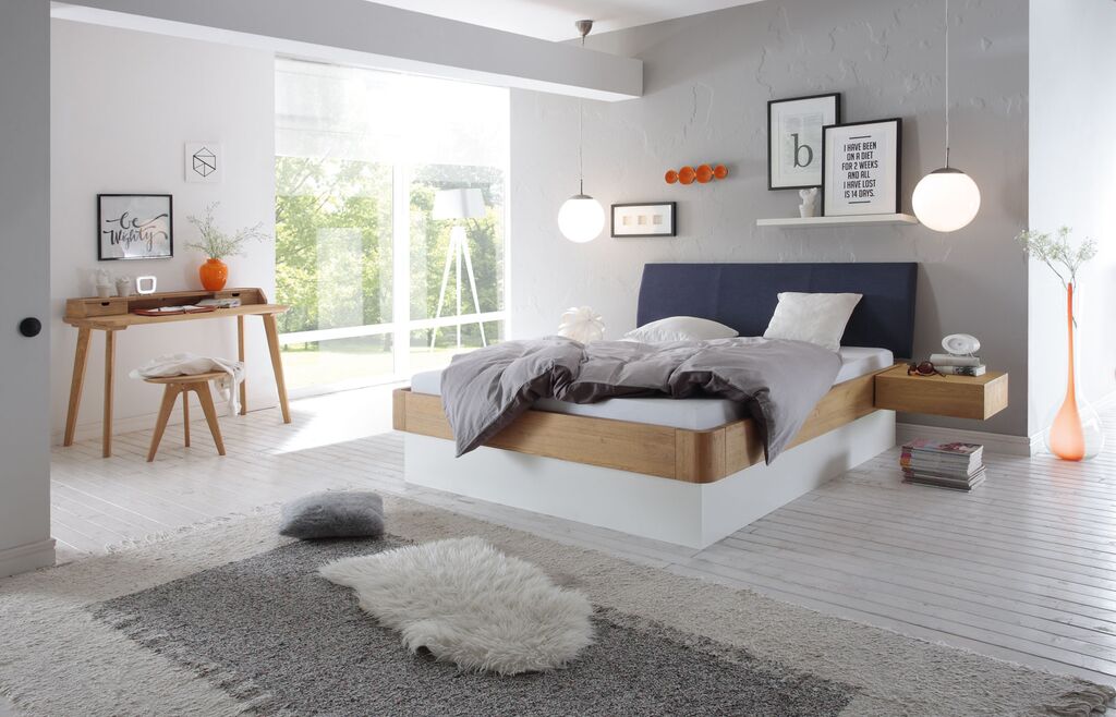 Hasena-Bett mit Holrahmen und weißem Unterbau und dunkelblauem Kopfteil in einem hellen Raum mit weißem Boden und hellen Teppichen