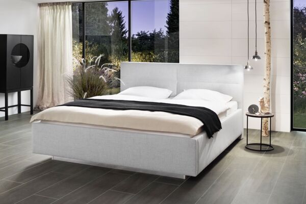 Hellgraues Stoffbett mit Wasserbettmatratze von Tasso in einem stimmungsvollen Raum mit Holzboden, großen Fenstern und indirekten Lichtquellen