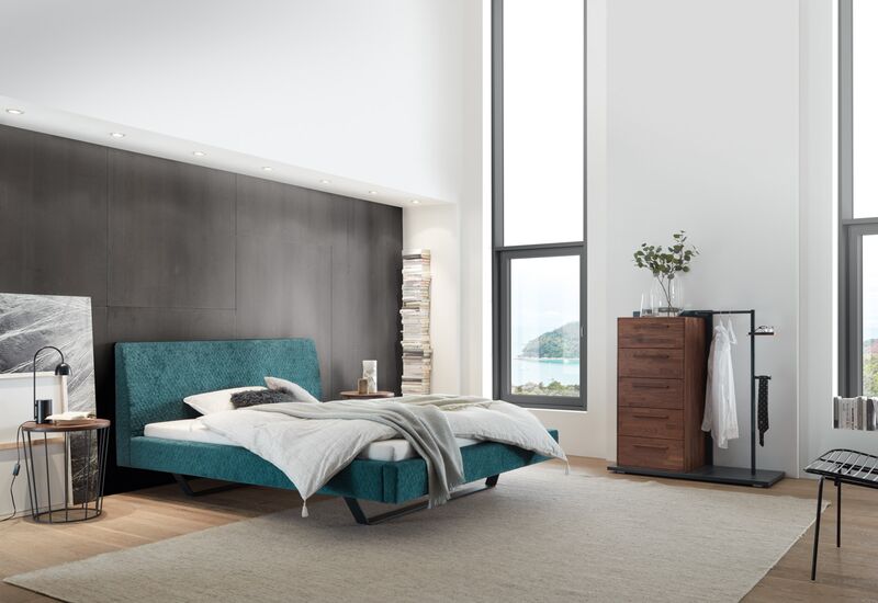 Türkises Polsterbett von Hasena aus der Dreamline-Kollektion in einem minimalistisch eingerichteten Zimmer mit sehr hohen, hellen Decken.
