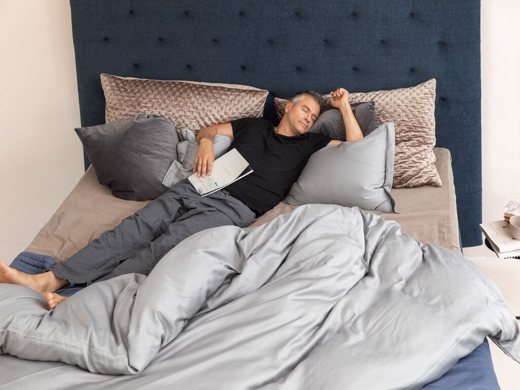 Ein Mann schläft entspannt im Bett, umgeben von weichen Kissen und einer gemütlichen Decke.