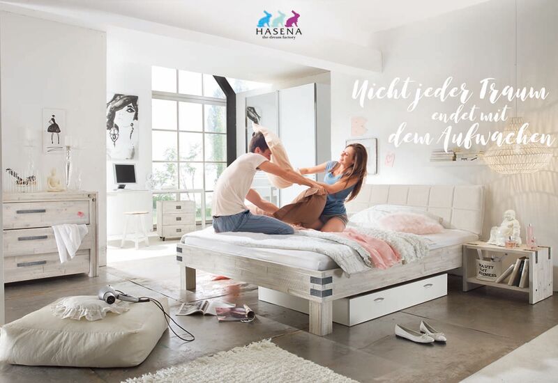 Ein Paar lacht und spielt auf einem modernen Bett in einem hellen Schlafzimmer mit stilvoller Dekoration.