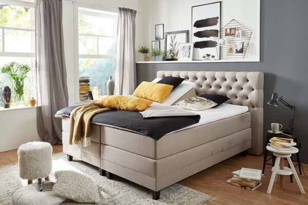 Beiges Boxspringbett mit Rautenheftung am Kopfteil und moderner Zimmereinrichtung