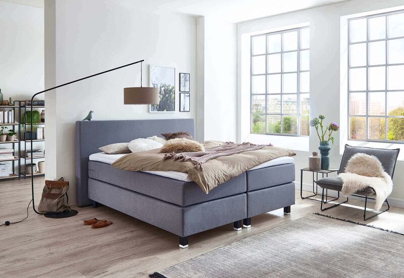 Ein modernes Schlafzimmer mit einem gemütlichen Bett, großen Fenstern und einem stilvollen Sessel im Hintergrund.