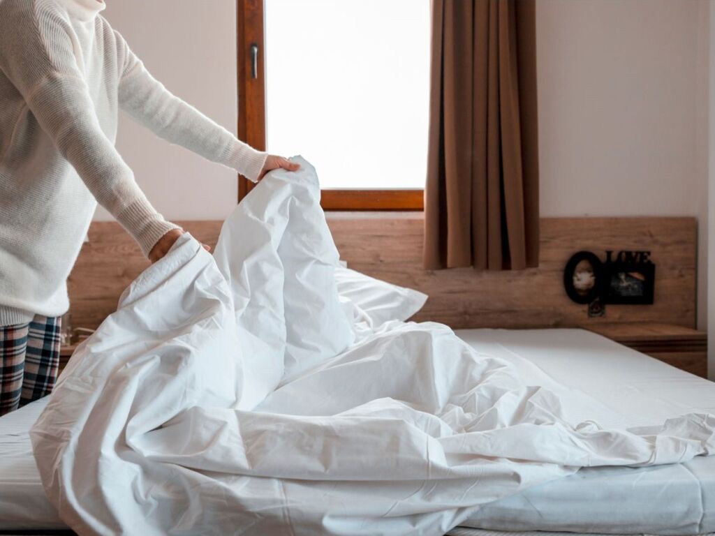 Eine Person bezieht ein Bett mit frischer Bettwäsche, um allergiebedingte Beschwerden zu vermeiden.