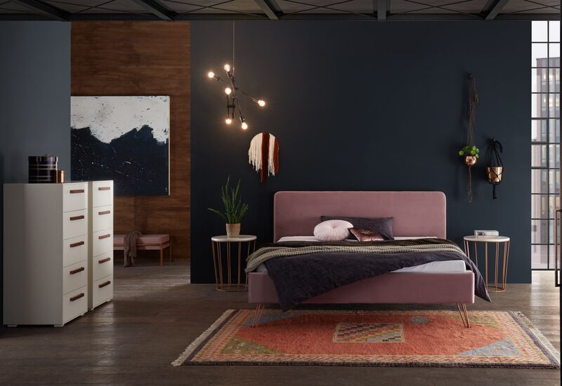 Polsterbett der Marke Hasena in altrose vor einer dunkelblauen Wand, stilvoll mit Pflanzen und Kommoden eingerichtetes Zimmer.