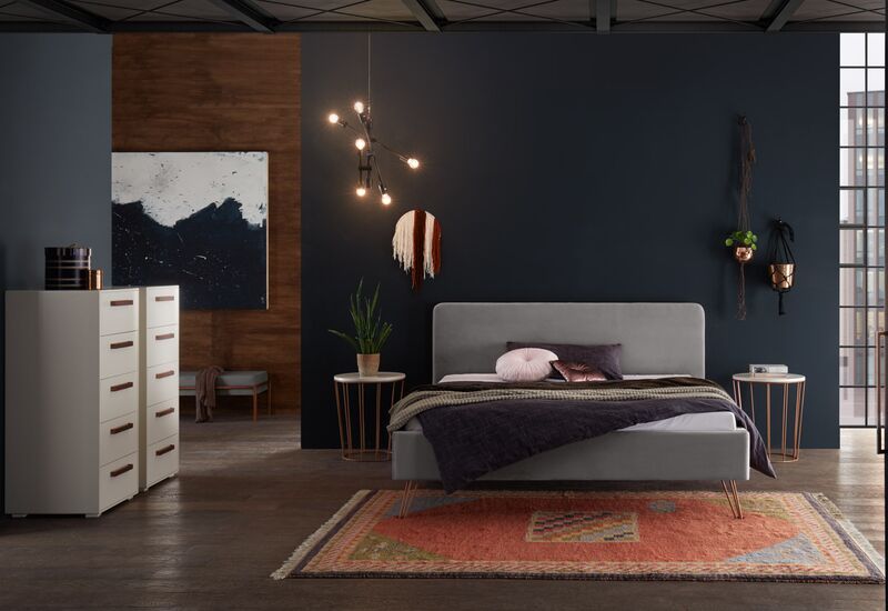 Ein graues Polsterbett von Hasena Dreamline steht vor einer dunkelblauen Wand, umgeben von dezenten Holztönen und indirektem Licht.