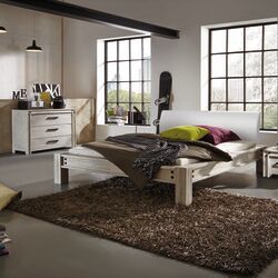Ein modernes Schlafzimmer mit einem hellen HasenA-Holzbett, bunten Kissen und einem braunen Langfloorteppich.