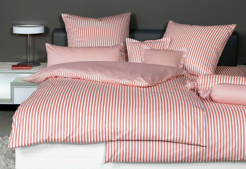 Weißes Bett mit rot-weißer Bettwäsche auf weißem Teppich