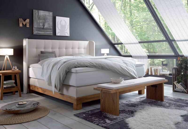 Hasena-Boxspringbett Massiva in hellbeige mit Holzanteil in einem Zimmer mit schrägen Dachfenstern.