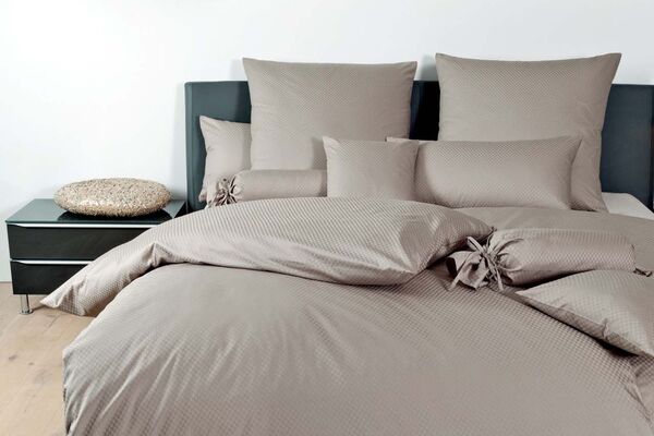 Ein modernes Schlafzimmer mit beigem Bettzeug und dekorativen Kissen, das Gemütlichkeit und Stil ausstrahlt.