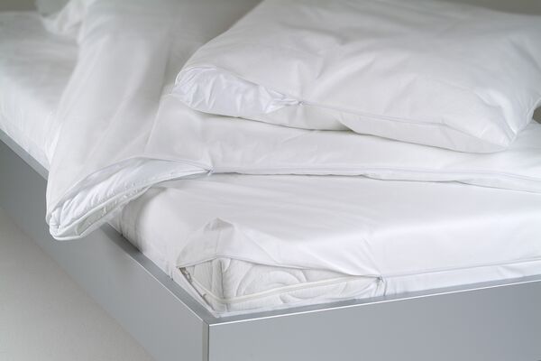 Ein modernes Bett mit frischer, weißer Bettwäsche und Kissen mit Reißverschluss, die ordentlich auf der Matratze liegen.