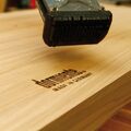 Ein Stück Holz wird mittels Stempel mit dem Schriftzug "dormiente made in Germany" versehen.