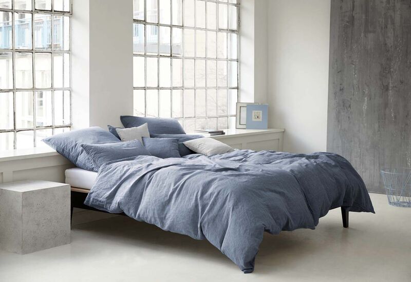 Ein schlichtes schwarzes Bett in einem Industrialstyle-Zimmer mit graublauer Joop-Bettwäsche