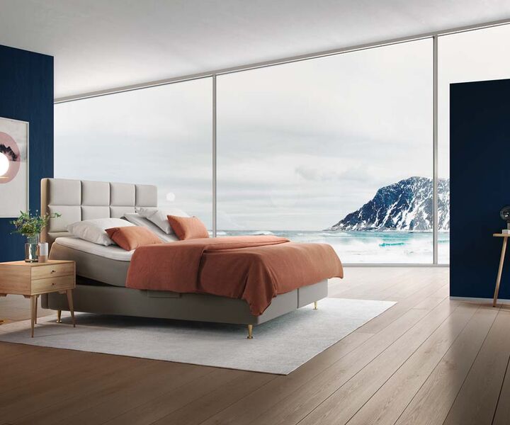 Ein modernes Schlafzimmer mit einem komfortablen Bett, orangefarbener Bettwäsche und Blick auf eine felsige Küstenlandschaft.