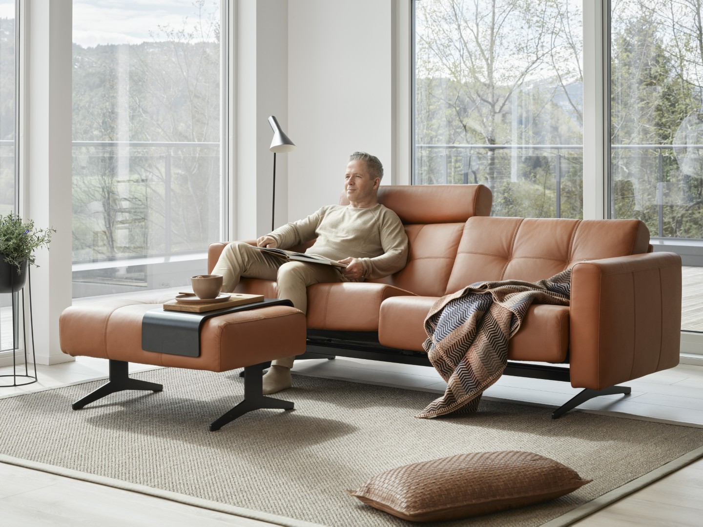 Mittlealter, lächelnder Mann sitzend auf einem cognac-farbenen Zweiersofa von Stressless mit passendem Fußteil,