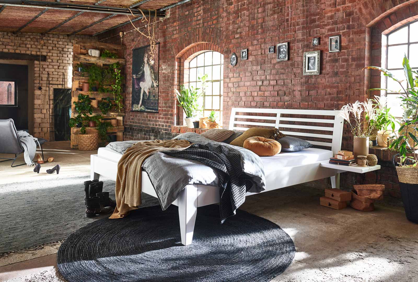 Ein weißes Bett aus Holz steht in einem Raum mit roten Backsteinwänden