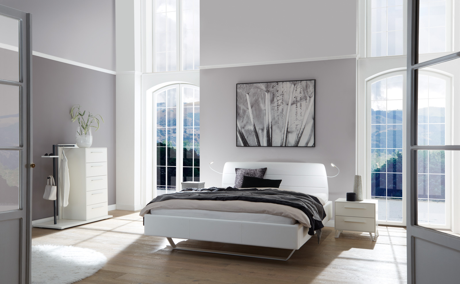 Weißes Hasena-Dreamline-Bett mit Metallfuß zwischen zwei großen, bodentiefen Fenstern.