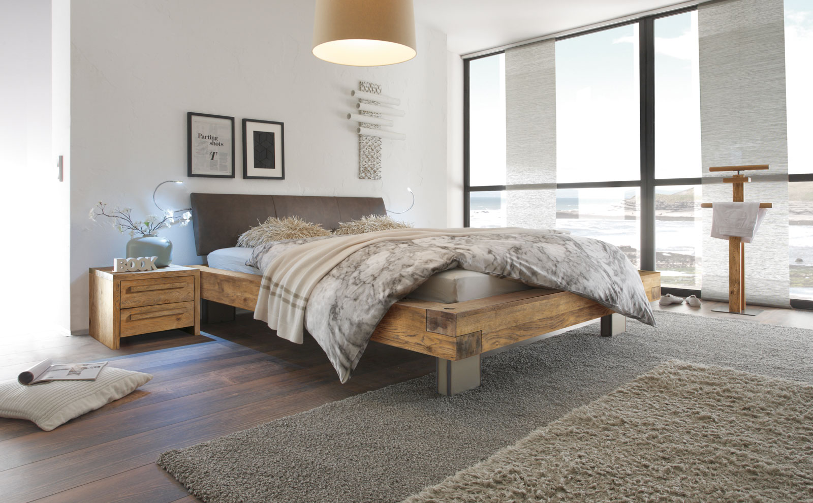 Ein modern gestaltetes Schlafzimmer mit einem Hasena-Holzbett, gemütlichen Kissen und großen Fenstern, die Licht hereinlassen.