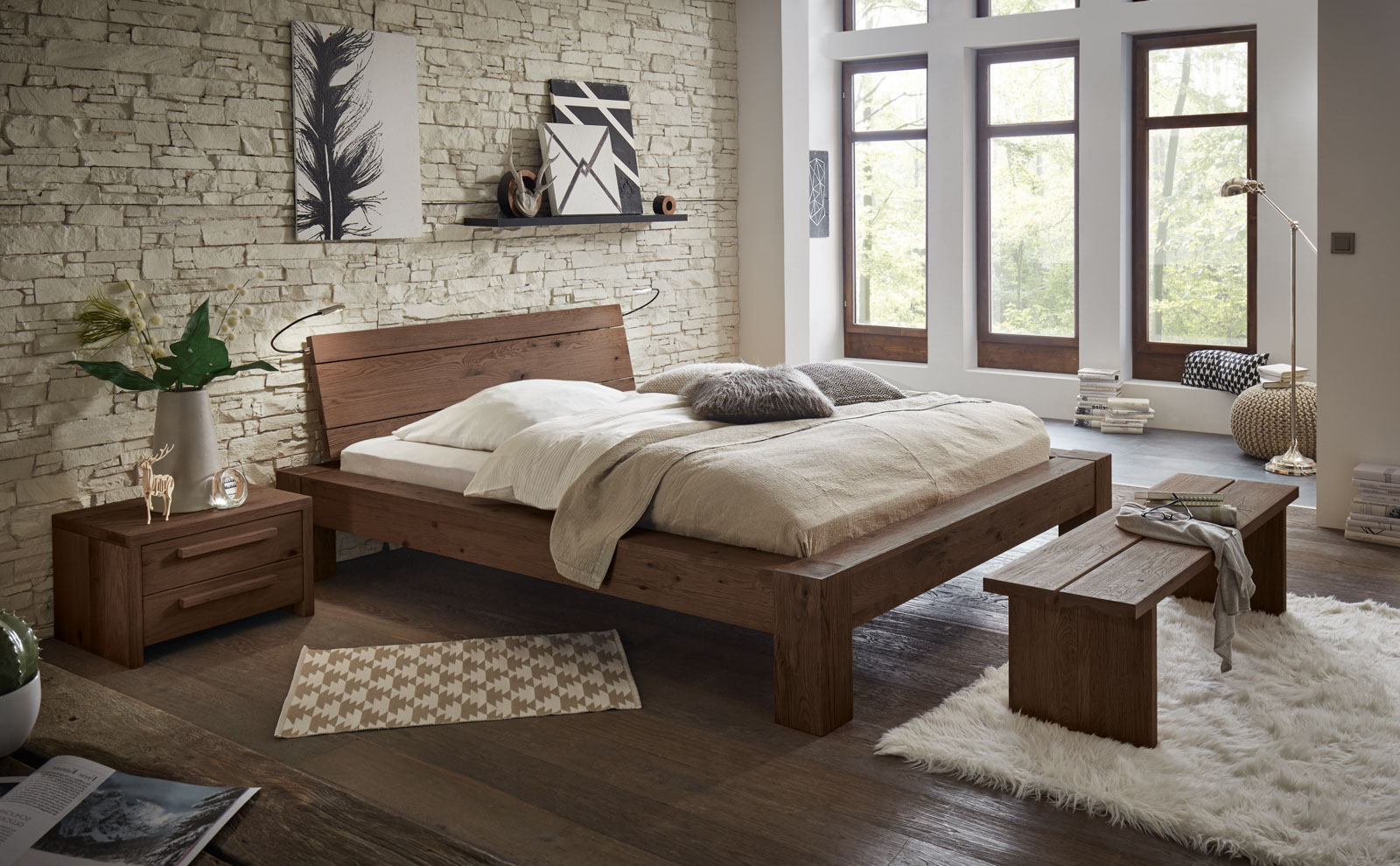 Bett der Oak Wild-Linie von Hasena mit beigen Bettwaren, passender Bank und Nachttisch in einem hellen Raum