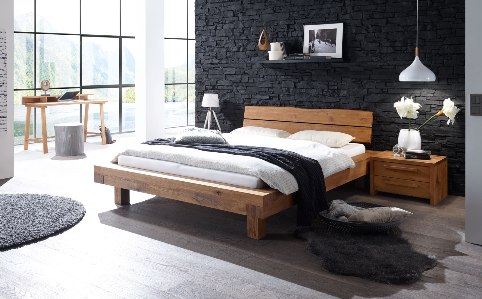 Ein Bett der Oak Wild-Serie von Hasena steht in einem hellen Raum vor einer schwarzen Steinwand