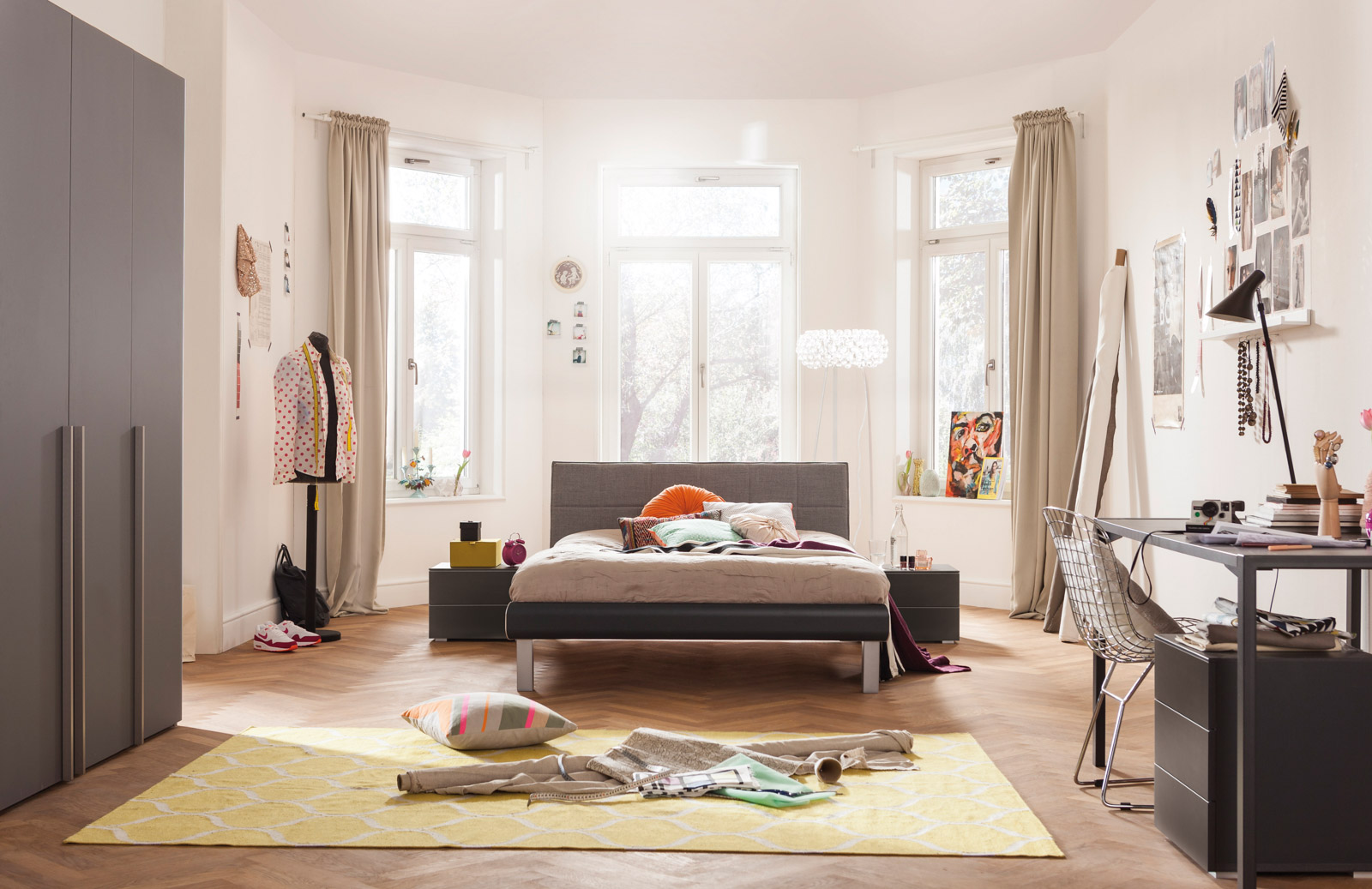 Bett aus der Soft Line-Reihe mit Polsterkopfteil in hellem Zimmer mit großen Fenstern und Vorhängen