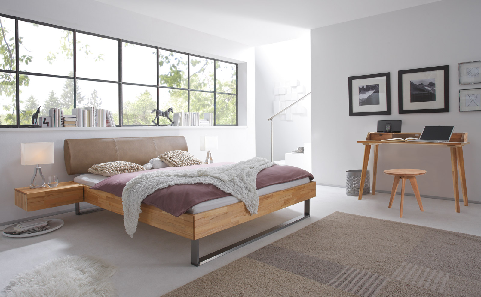 Hasena-Woodline-Bett aus Massivholz mit schwebenden Nachttischen, kleinem Schreibtisch und Hocker in einem weißen Raum mit großen Fenstern