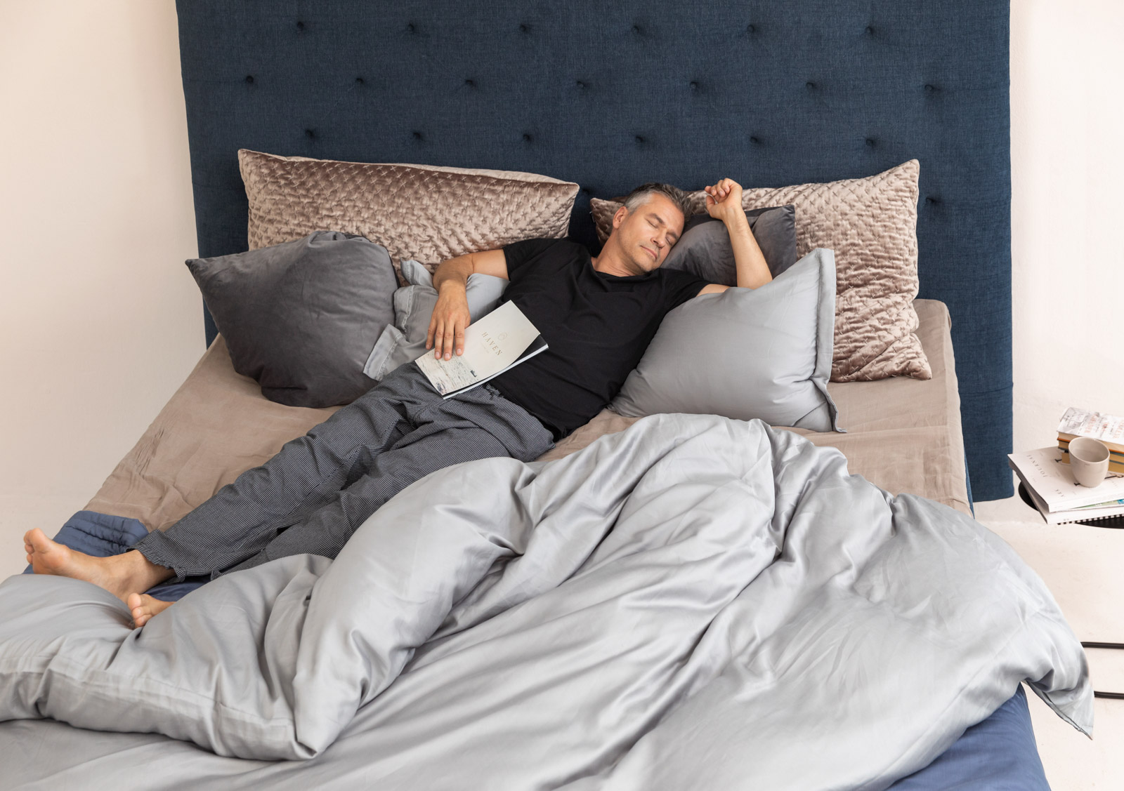 Ein Mann schläft entspannt im Bett, umgeben von weichen Kissen und einer gemütlichen Decke.