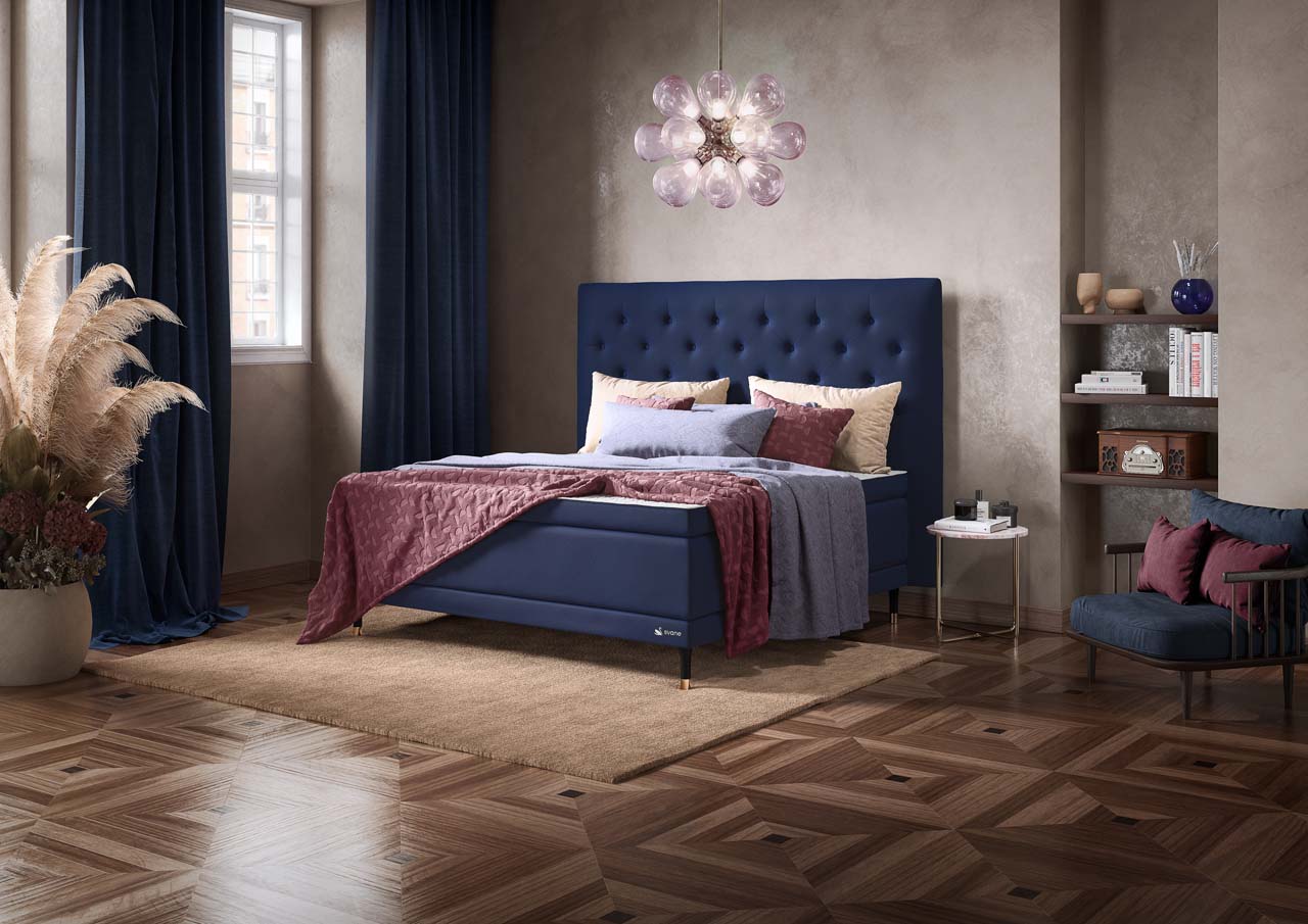 Ein luxuriös anmutendes Schlafzimmer mit einem dunkelblauen Svane-Zincere-Bett und passenden Vorhängen und einem dunklen Holzboden