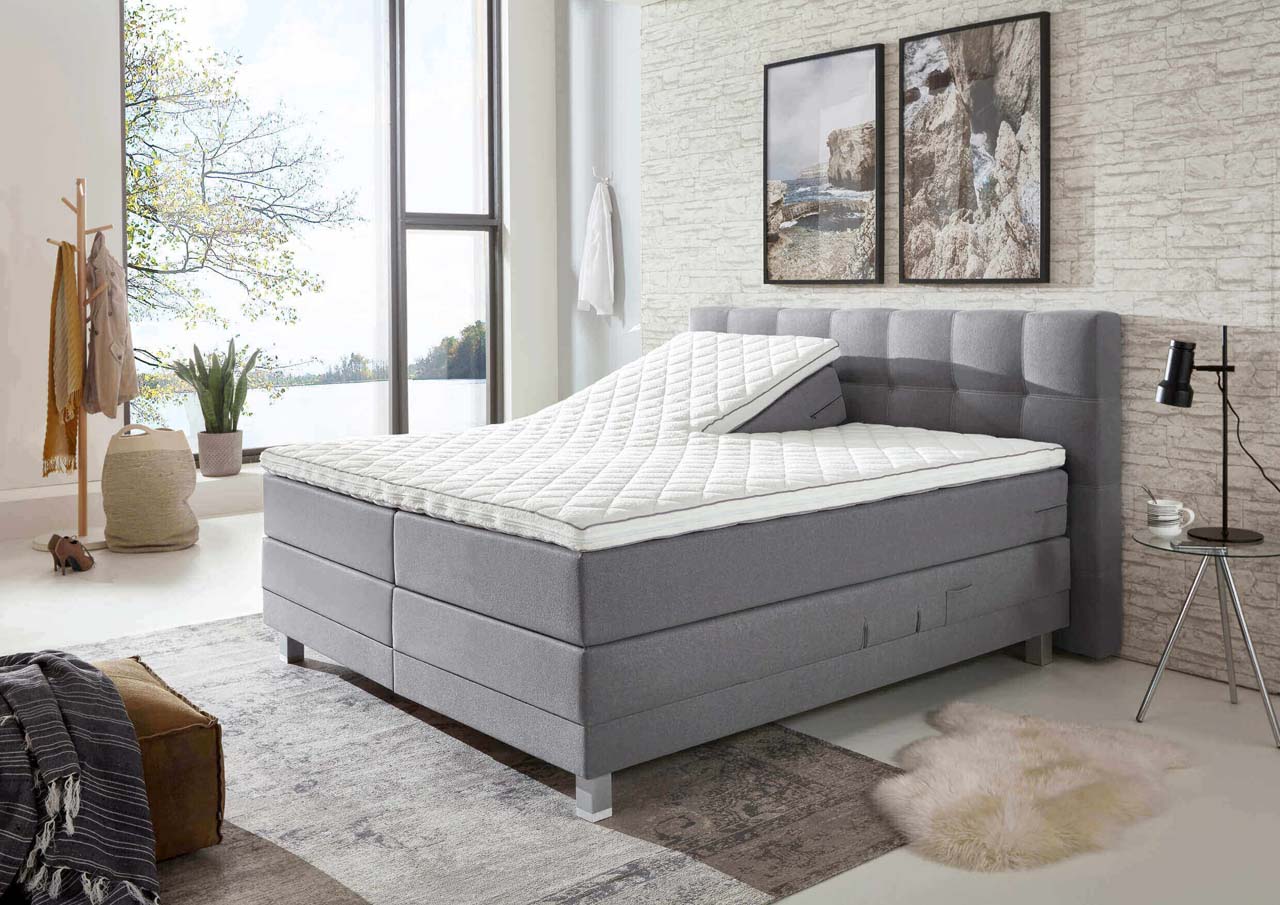 Graues Boxspringbett mit verstellbarem Lattenrost in einem gemütlich eingerichteten Schlafzimmer.