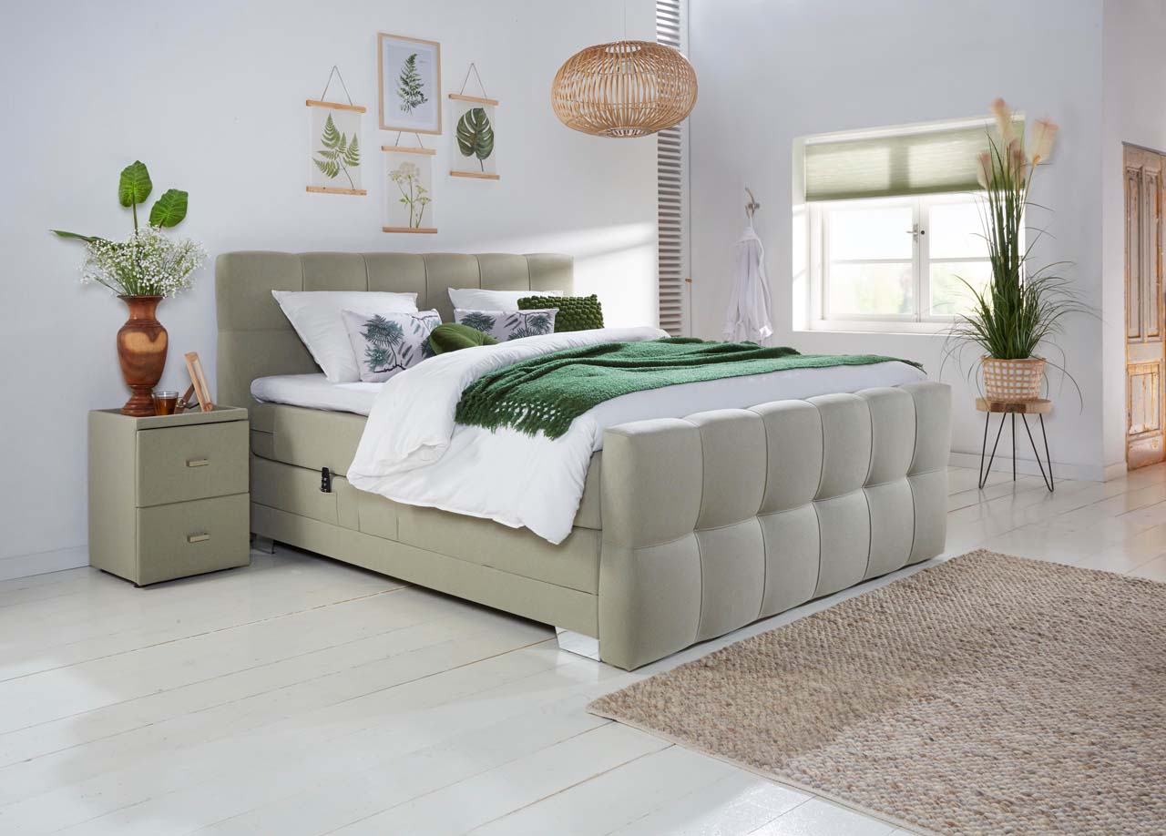 Ein modernes Schlafzimmer mit einem gepolsterten Bett, grünen Decken und Pflanzen schafft eine gemütliche Atmosphäre.