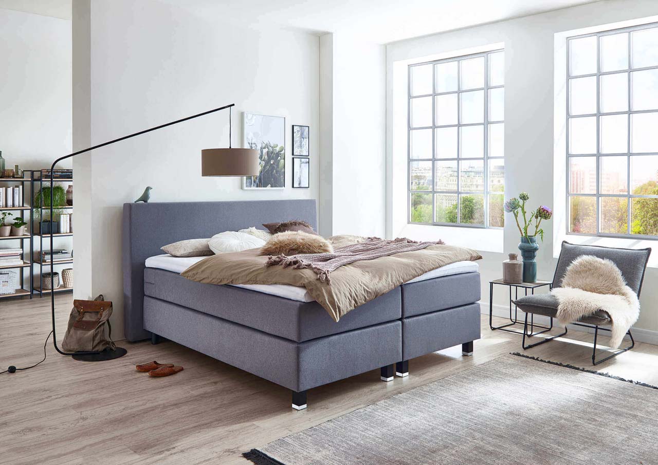 Ein modernes Schlafzimmer mit einem gemütlichen Bett, großen Fenstern und einem stilvollen Sessel im Hintergrund.