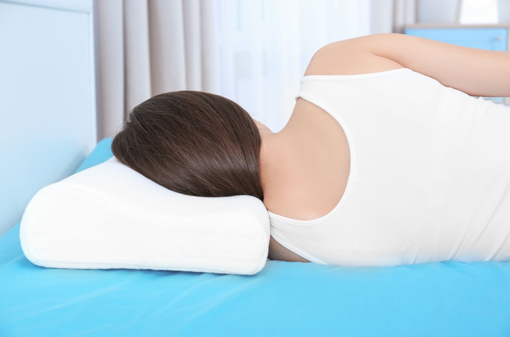 Eine Frau schläft seitlich auf einem blauen Bett mit einem ergonomischen Kissen für optimalen Schlafkomfort.