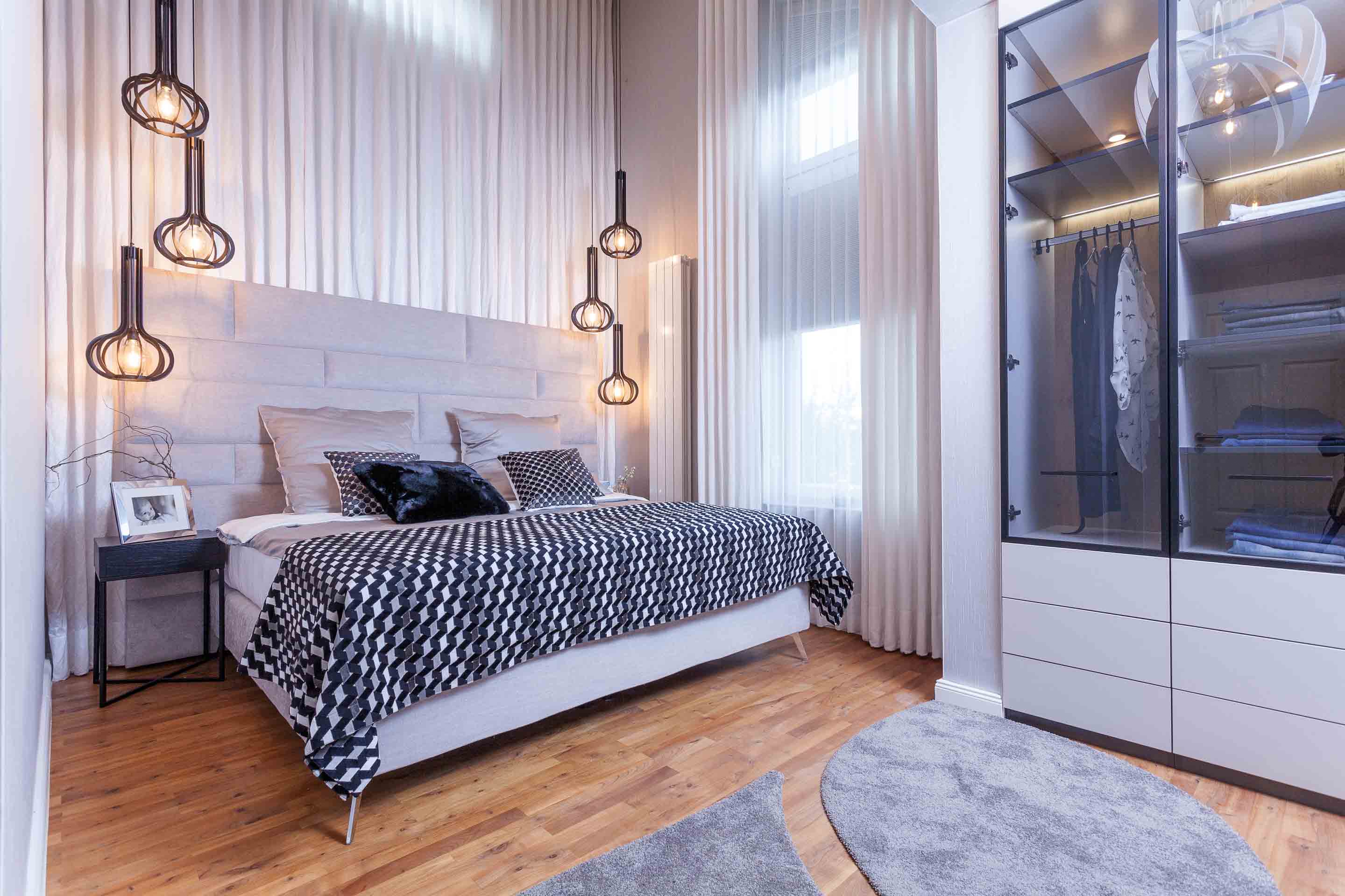 Beiges Polsterbett mit gemusterter Decke in einem beigen Schlafzimmer mit Kleiderschrank