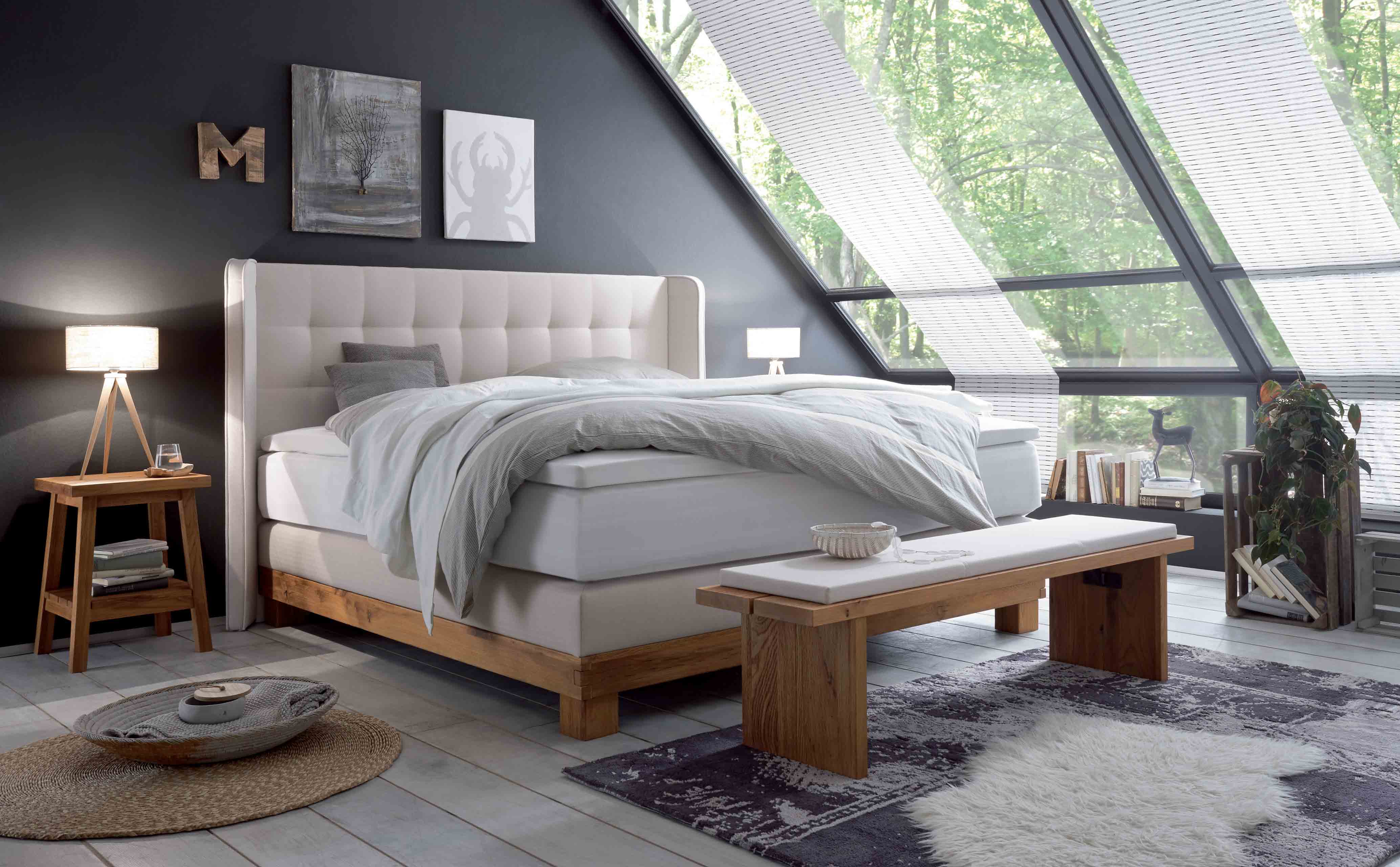 Hasena-Boxspringbett Massiva in hellbeige mit Holzanteil in einem Zimmer mit schrägen Dachfenstern.